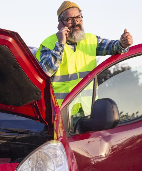 Adult man looking calm and talking on the phone on the side of the road. Latino man with hood open due to mechanical problem